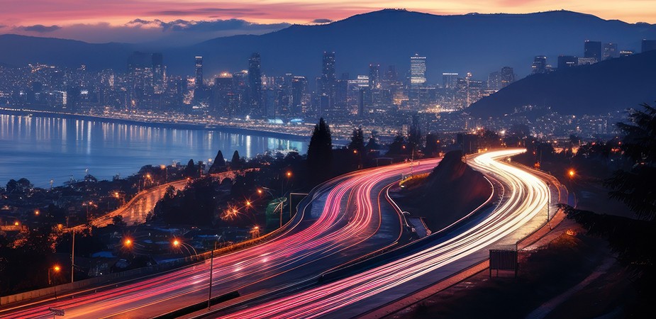 stream of lights on freeway at sunset with bay and skyscrapers in background