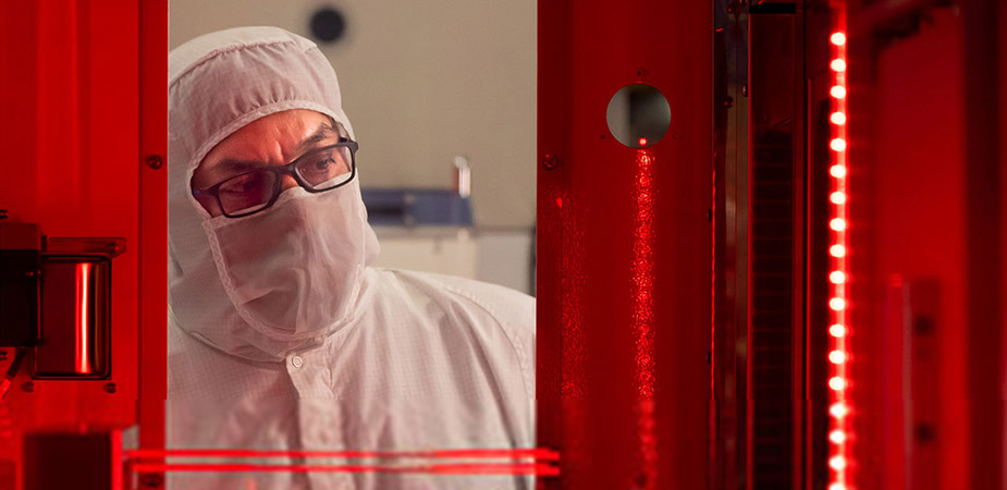 Person wearing a white clean room body suit and mask and looking into the room lit with red light
