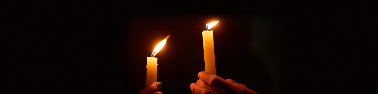 Two hands holding a lit candle in the dark