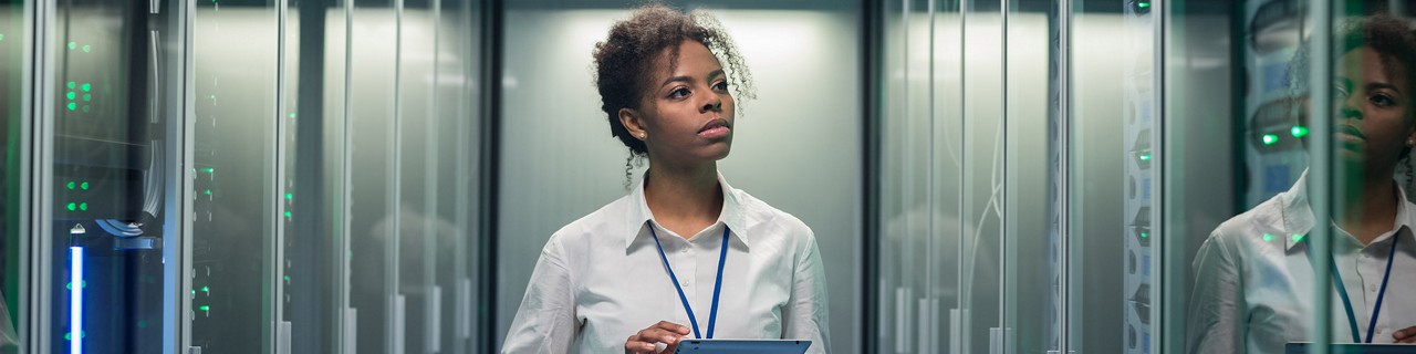 African American woman using tablet while walking in corridor of data center and checking hardware on server racks