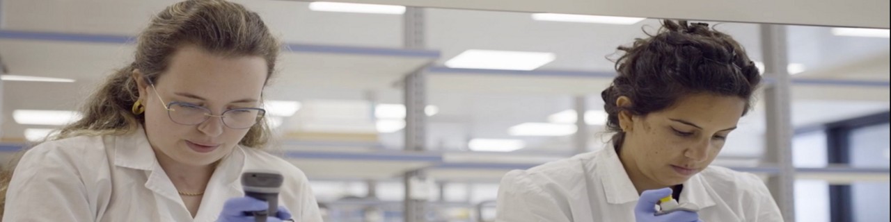 ventures-blog-hero-2000x500.jpg: Two women with white lab coats, one with a microscope