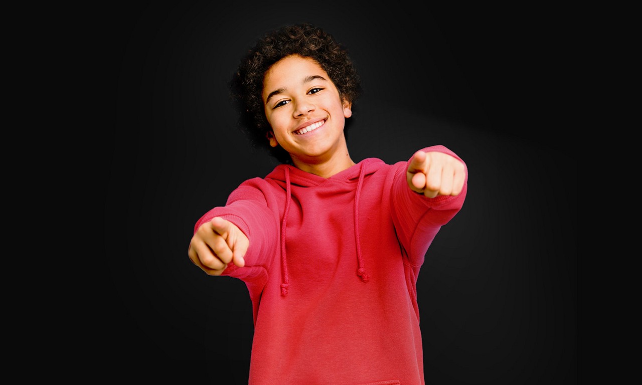 Smiling young person in a red hoodie pointing to camera