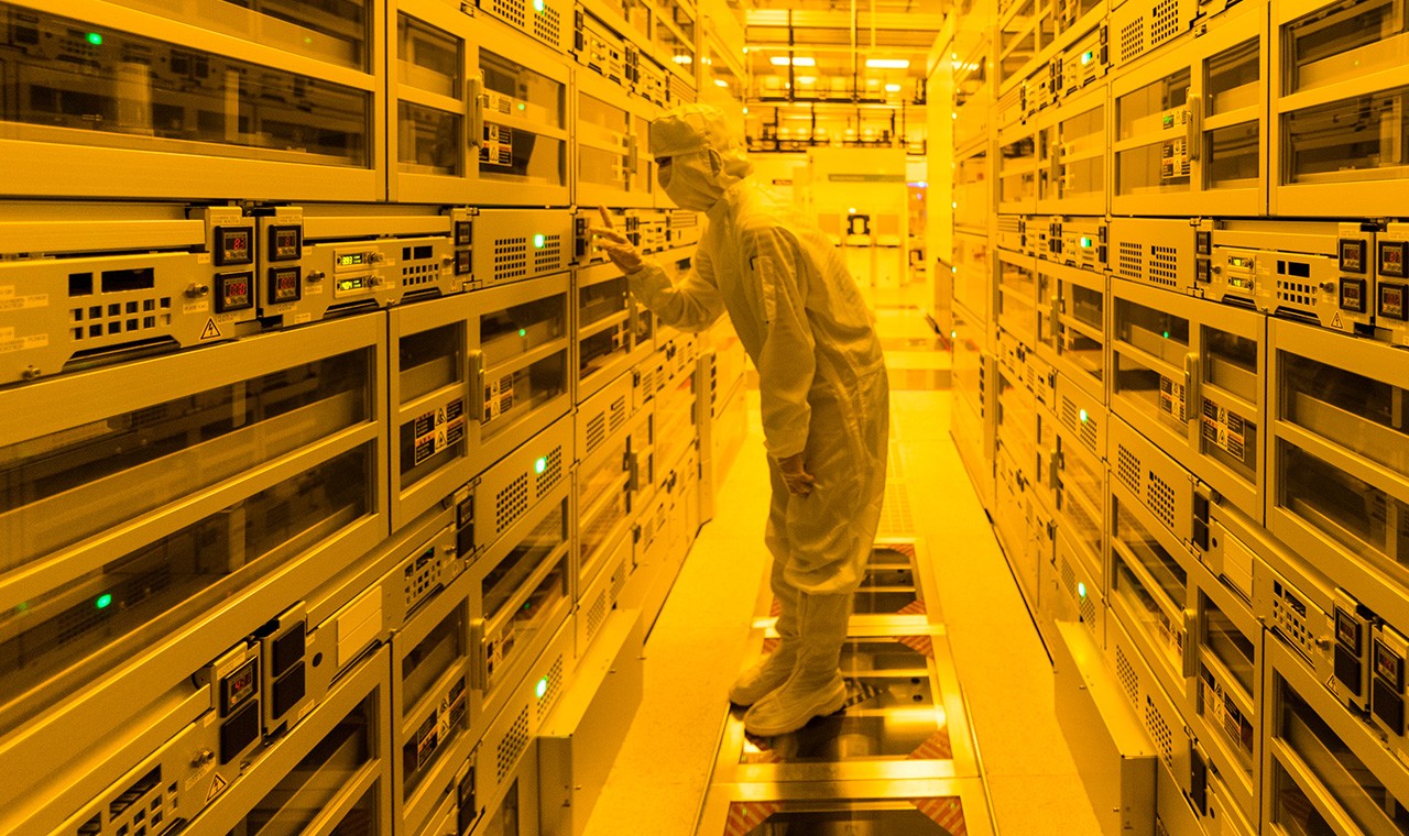 Workers in a fabrication clean room suit looking into a work area