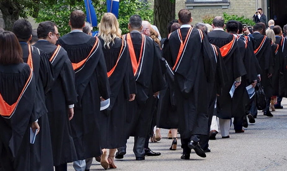 Graduation ceremony. Line of graduates walking towards building.