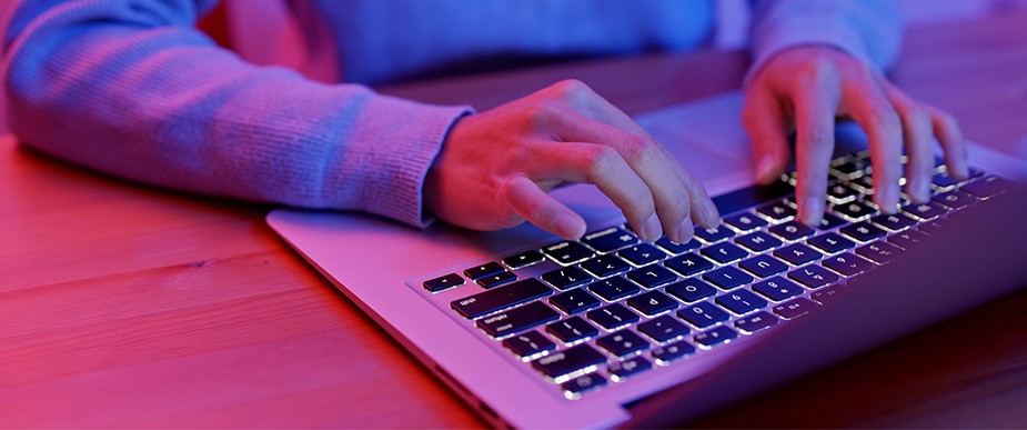 Close up of hands using a laptop keyboard in red and blue lighting